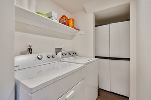 A laundry room with two front-loading washers and dryers, a shelf with laundry supplies, and a storage closet with sliding doors.