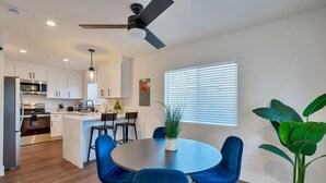 Une cuisine moderne avec des meubles blancs, un coin repas avec des chaises bleues et un ventilateur de plafond.
