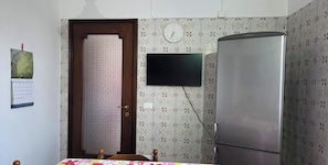 Quarto com cama, televisão na parede, frigorífico, porta e papel de parede estampado.