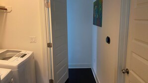 A laundry room with a washer and dryer, a hallway with a door, and a painting on the wall.