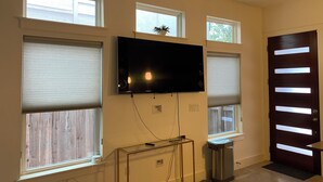 A room with a flat-screen TV mounted on the wall, a trash can, and a door with a modern design.