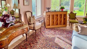 A room with a large window, a wooden cabinet, a chair, and a patterned rug. - Dream house by a Pond, 3-bed home in Woodridge NY w/ WiFi, AC, embraced by trees (Woodridge)