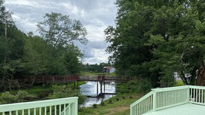 A wooden deck with a pond and a bridge in the background. - Dream house by a Pond, 3-bed home in Woodridge NY w/ WiFi, AC, embraced by trees (Woodridge)