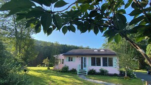 A single-story house with a pink exterior, a front porch, and a small garden area. - Dream house by a Pond, 3-bed home in Woodridge NY w/ WiFi, AC, embraced by trees (Woodridge)
