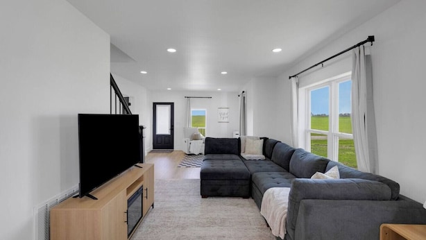 A modern living room with a large sectional sofa, a flat-screen TV, and a view of a green field through large windows. - Charming-relaxing 3BR farmhouse *15min from town (Oblong)