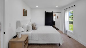A bedroom with a bed, bedside table, lamp, and a view of the outdoors. - Charming-relaxing 3BR farmhouse *15min from town (Oblong)