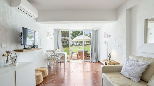 En moderne stue med TV, sofa, spisebord og stole. Der er en stor skydedør til en terrasse med parasol.