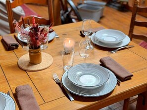 A wooden dining table set with plates, glasses, a candle, and a decorative vase. - En Pascot - LAGARDE - Vacation Home (LAGARDE)