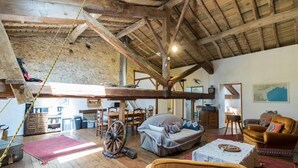 A rustic interior with exposed wooden beams, a large wooden table, and a cozy seating area with a sofa and armchairs.