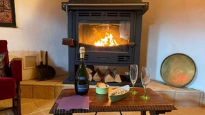 A cozy room with a wood-burning stove, a bottle of wine, a bowl of nuts, and two glasses on a table.