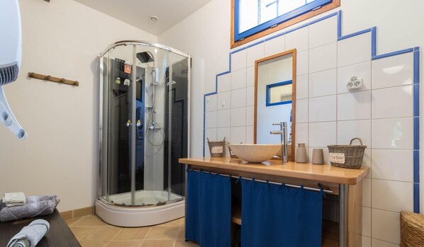 Un baño con ducha de vidrio, tocador de madera con lavabo y un espejo sobre el lavabo.