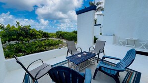 Une terrasse avec une table et des chaises, une petite table avec des chaises, et une vue sur la verdure et un bâtiment.