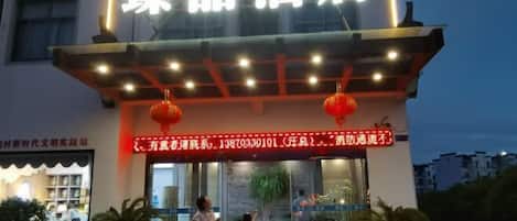 A hotel entrance with a neon sign, a red lantern, and a glass door.
