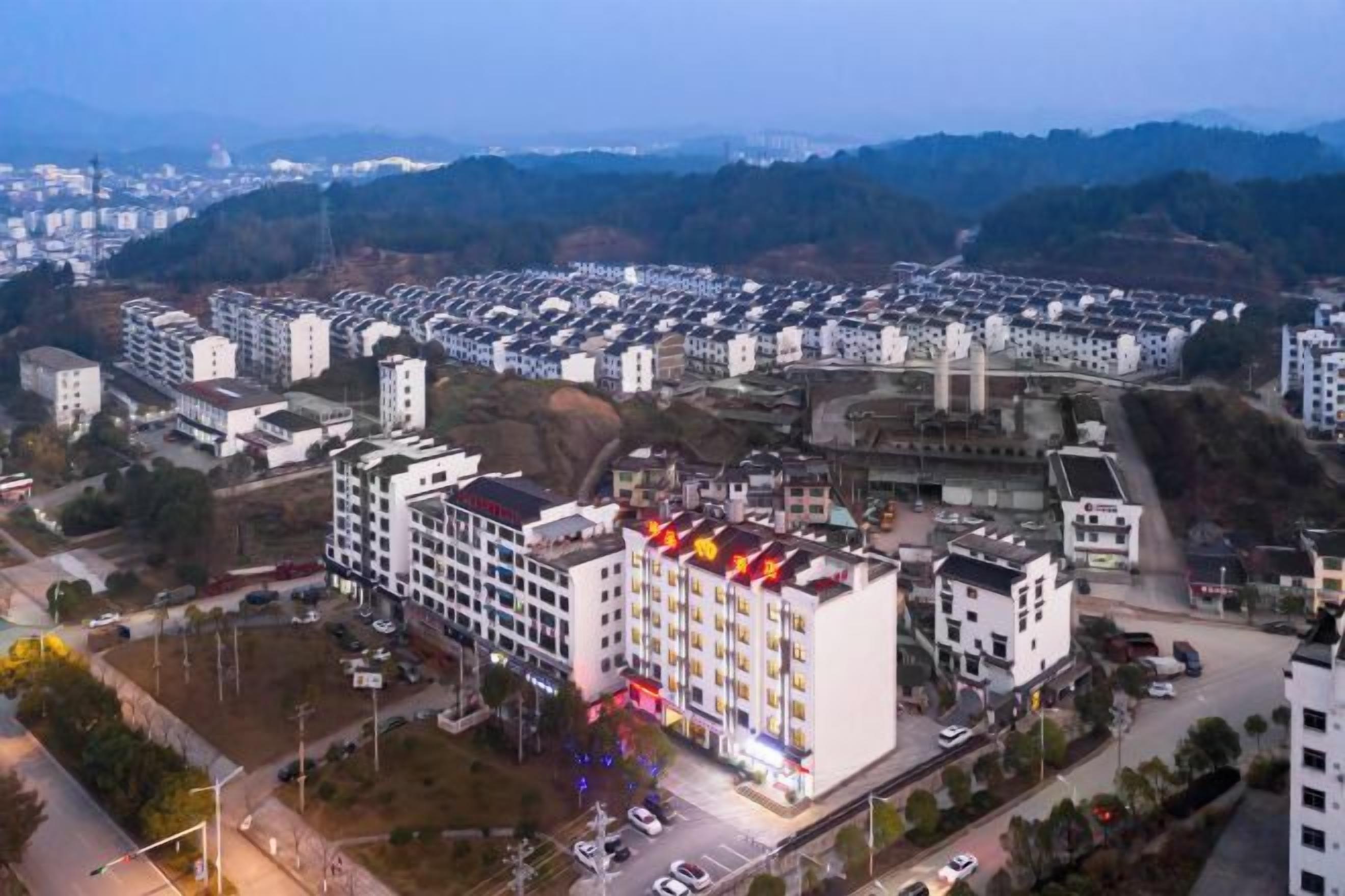 A multi-story hotel with a central courtyard, surrounded by residential buildings, and a bridge in the background.