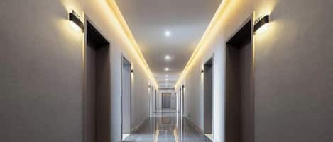 Un pasillo largo y estrecho con puertas a ambos lados, iluminado por luces en el techo.