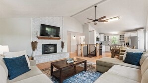 A spacious living room with a fireplace, a dining area, and a kitchen.
