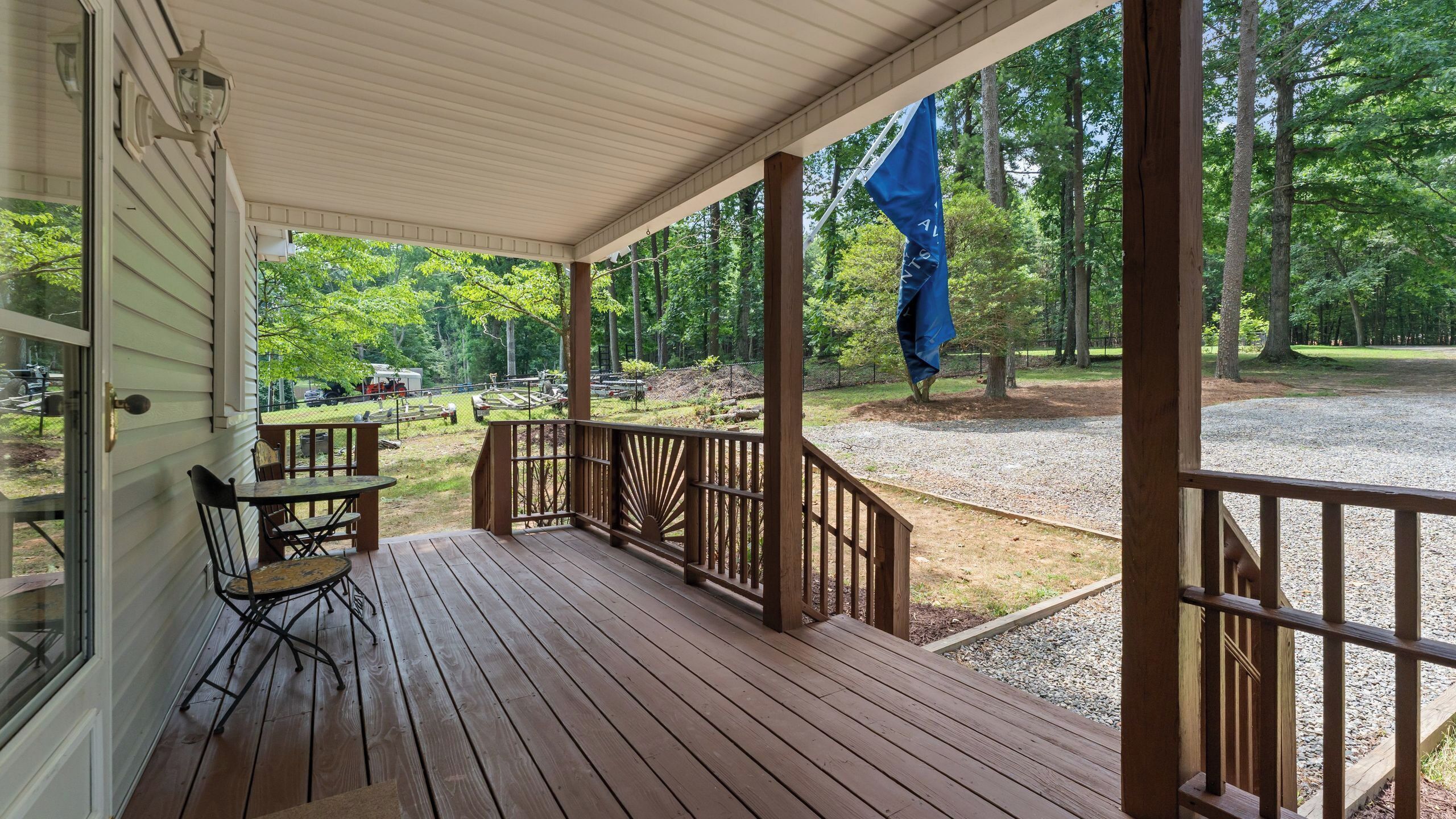 A wooden deck with a table and chairs, a covered porch, and a view of a forested area.