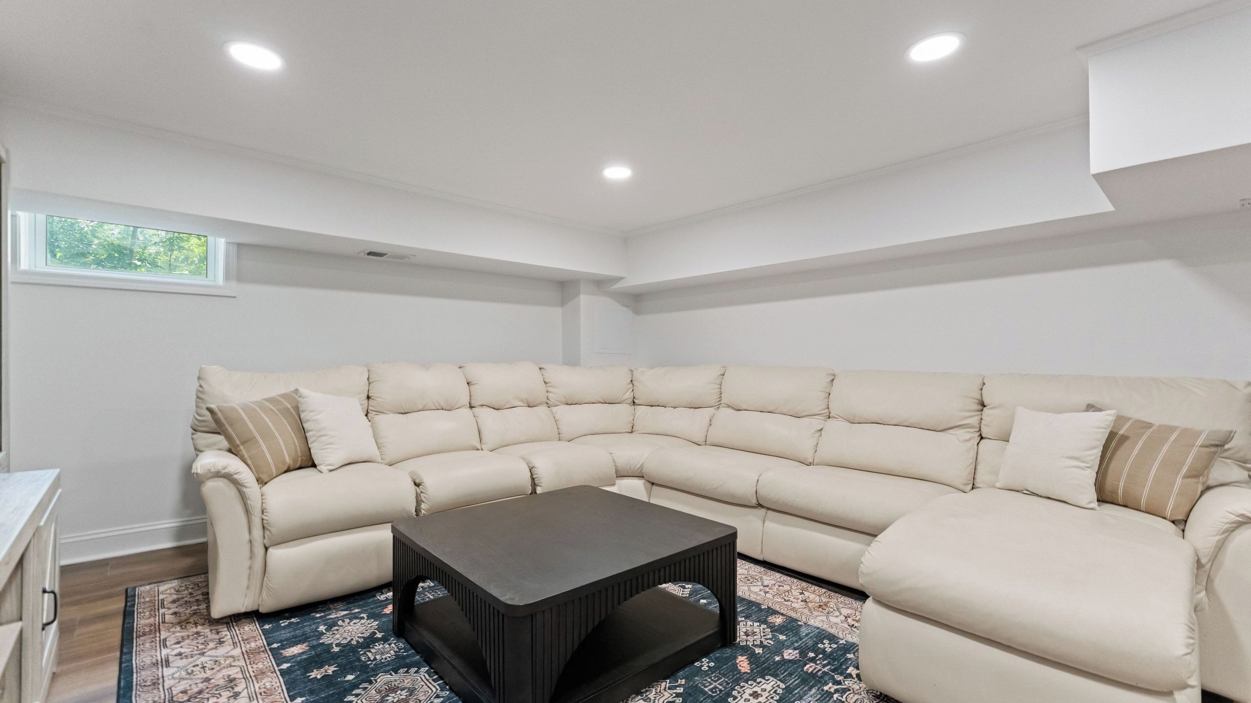 Una sala de estar moderna con un sofá seccional color beige, una mesa de centro oscura y alfombras estampadas.