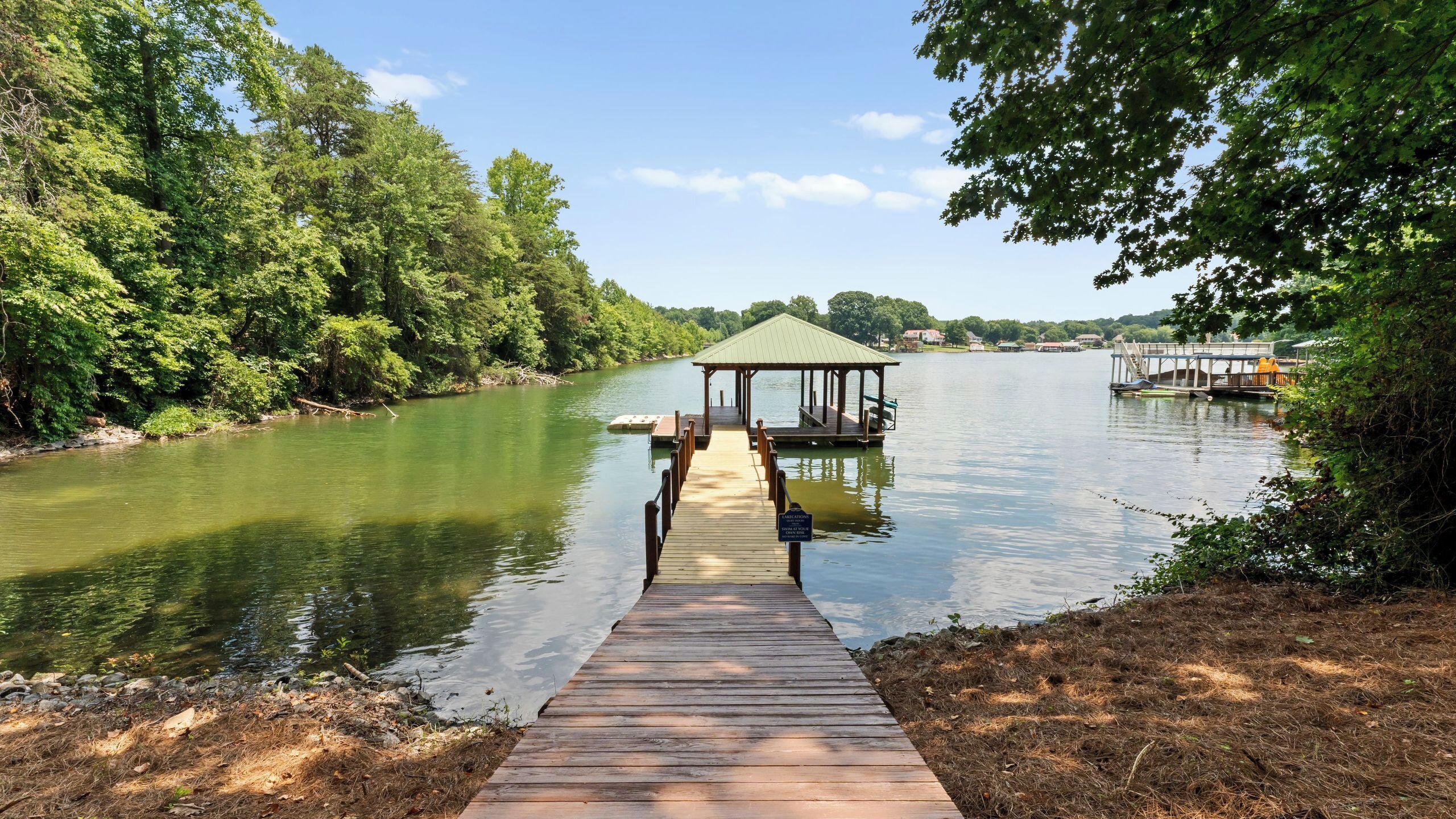 Een houten steiger die uitkomt bij een prieeltje aan een rustige rivier, omringd door weelderige begroeiing.