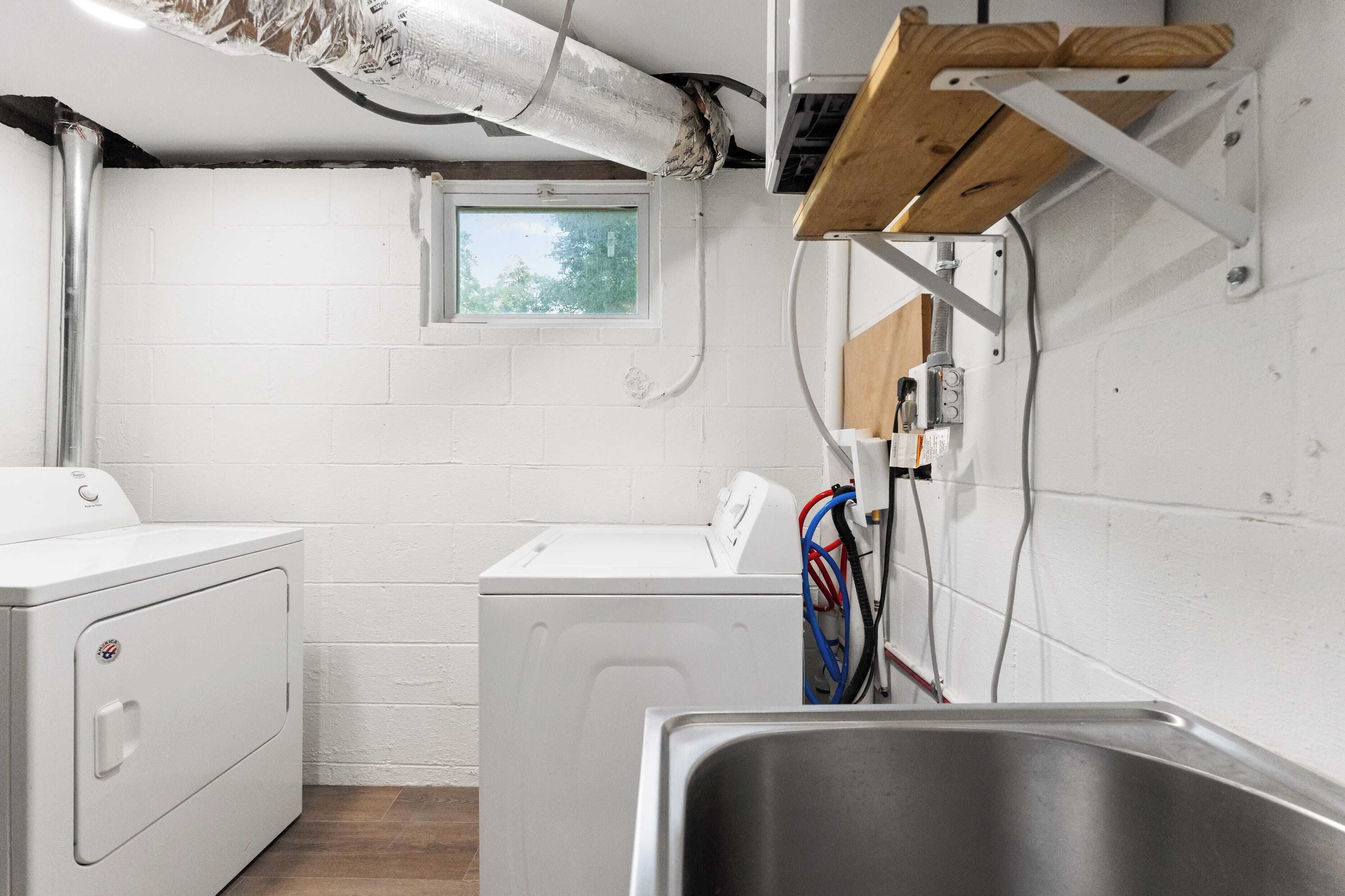 A laundry room with two white washing machines, a window, and a metal sink.