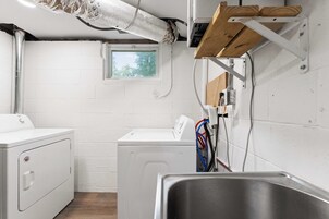 A laundry room with two white washing machines, a window, and a metal sink.