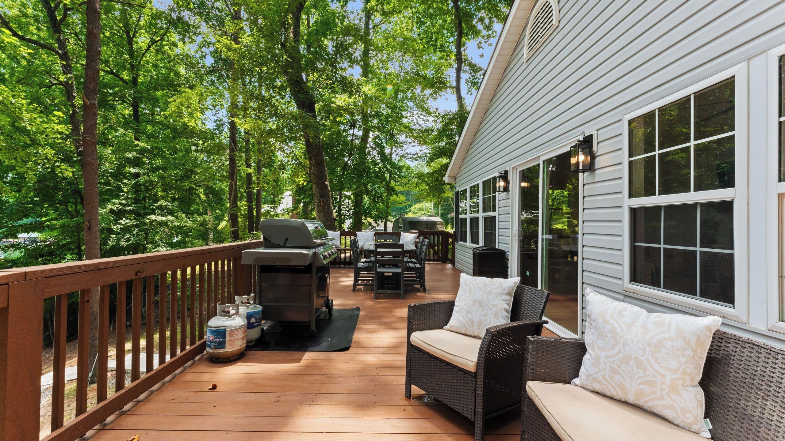 A covered deck with outdoor furniture, a grill, and a barbecue.
