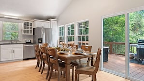 A modern kitchen with white cabinets, a dining table set for six, and a deck with a grill.