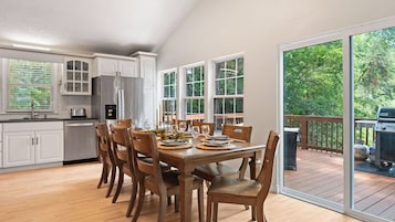 Una cocina moderna con armarios blancos, una mesa de comedor preparada para seis personas y una terraza con una parrilla.