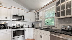 A modern kitchen with white cabinetry, stainless steel appliances, and a black countertop.