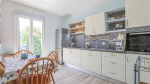 Een moderne keuken met witte kasten, een inbouwoven en een eethoek met een tafel en stoelen.