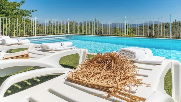 Un espace aménagé au bord de la piscine, avec des chaises longues blanches, une petite pile de paille et des serviettes.