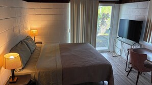 A hotel room with a bed, a desk with a chair, a television, and a window with curtains. - Charming 2-bedroom house in wonderful Pāhoa with free private covered parking (Pāhoa)