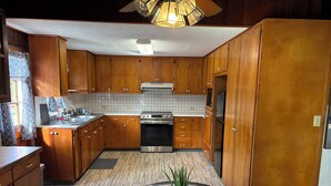 A modern kitchen with wooden cabinets, a stainless steel oven, and a glass-top dining table with a potted plant. - Charming 2-bedroom house in wonderful Pāhoa with free private covered parking (Pāhoa)