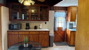 A kitchen with wooden cabinets, a microwave, a coffee maker, and a glass table with a potted plant. - Charming 2-bedroom house in wonderful Pāhoa with free private covered parking (Pāhoa)