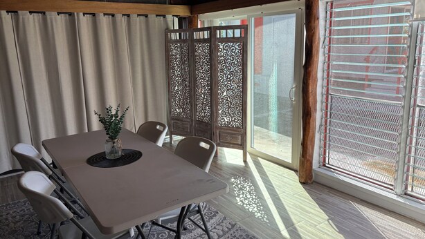 A dining area with a table, chairs, a vase with greenery, a ceiling fan, and a sliding glass door with a view. - Charming 2-bedroom house in wonderful Pāhoa with free private covered parking (Pāhoa)