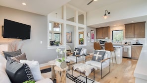 A modern living room with a sofa, armchairs, a coffee table, and a dining area with chairs and a kitchen in the background.