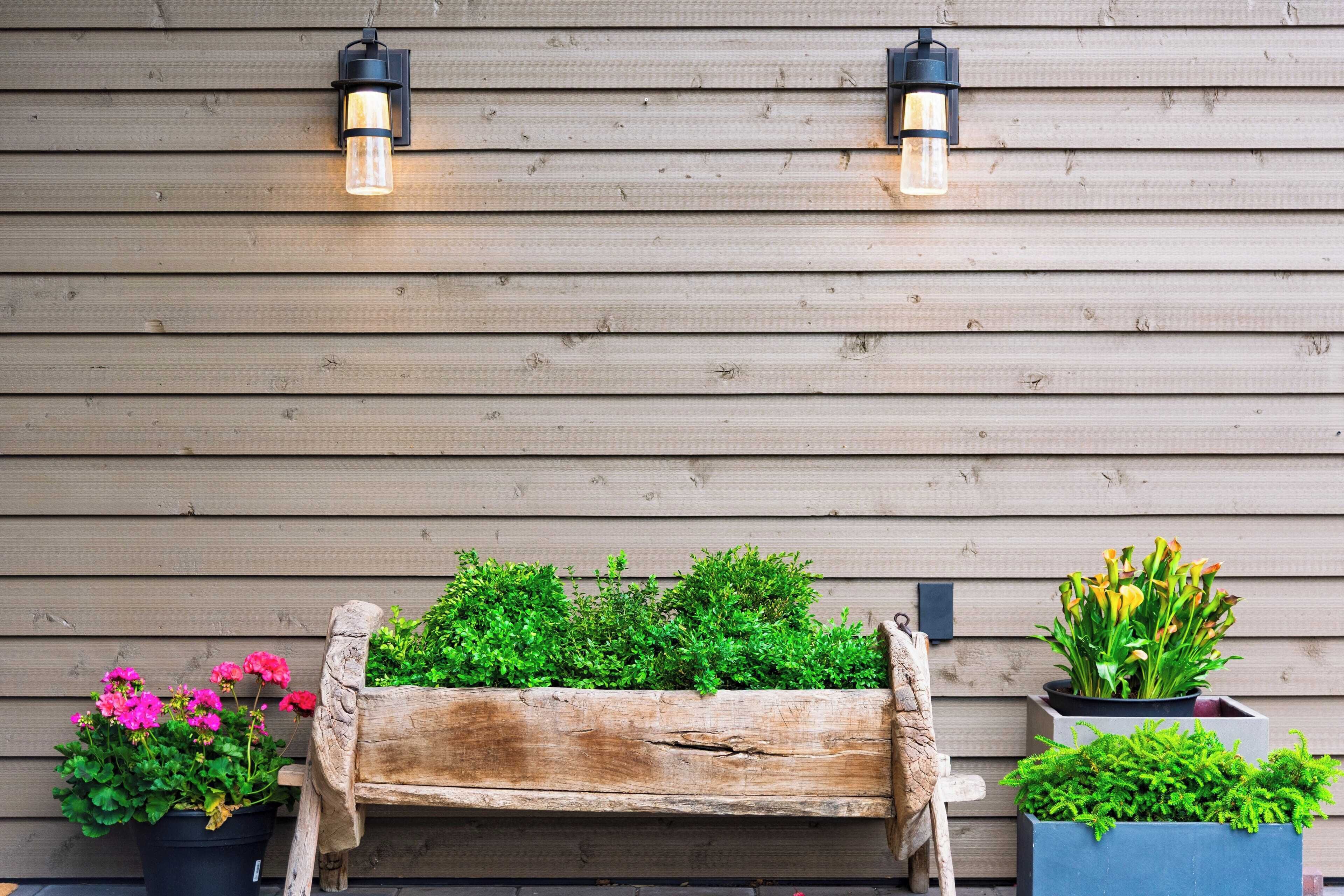 Un banco de madera con una jardinera frente a un muro de madera con dos luces empotradas.