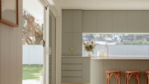 Una cocina moderna con un amplio ventanal, taburetes de madera y vistas al jardín trasero.