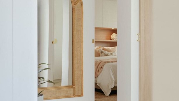 Un dormitorio con un espejo grande, una cama con ropa blanca y suelo de madera.
