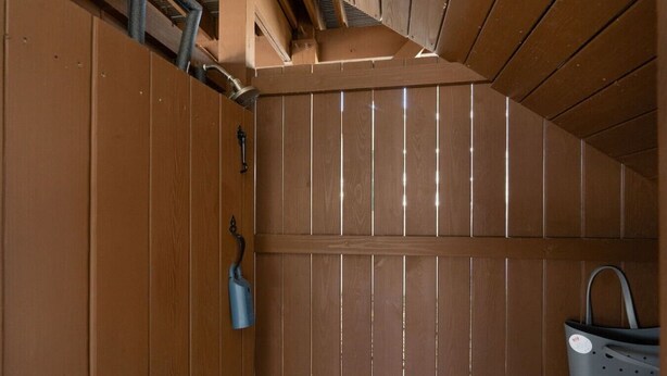 A wooden room with a shower, a blue faucet, and a gray plastic basket.