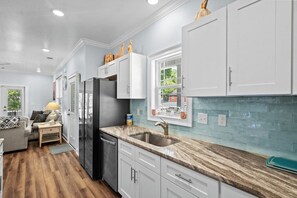 A modern kitchen with white cabinets, a marble countertop, and a window overlooking the outdoors.