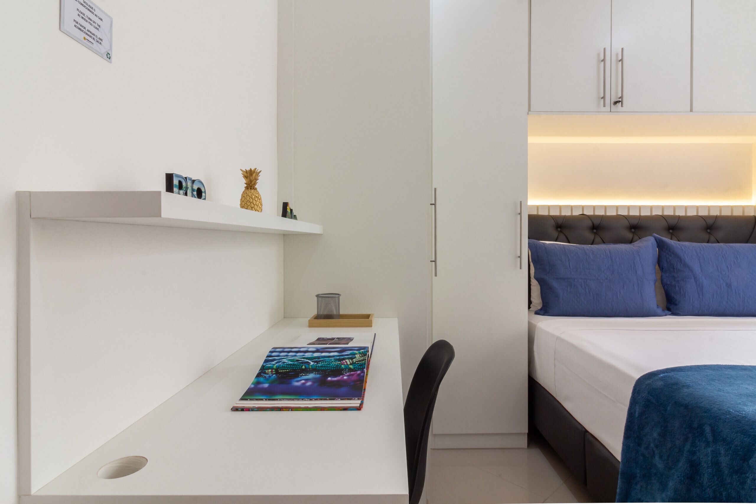 A modern hotel room with a bed, a desk, and a shelf with decorative items.