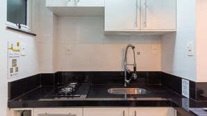 Une cuisine moderne avec des meubles blancs, un plan de travail noir, une cuisinière à gaz et un évier en acier inoxydable.