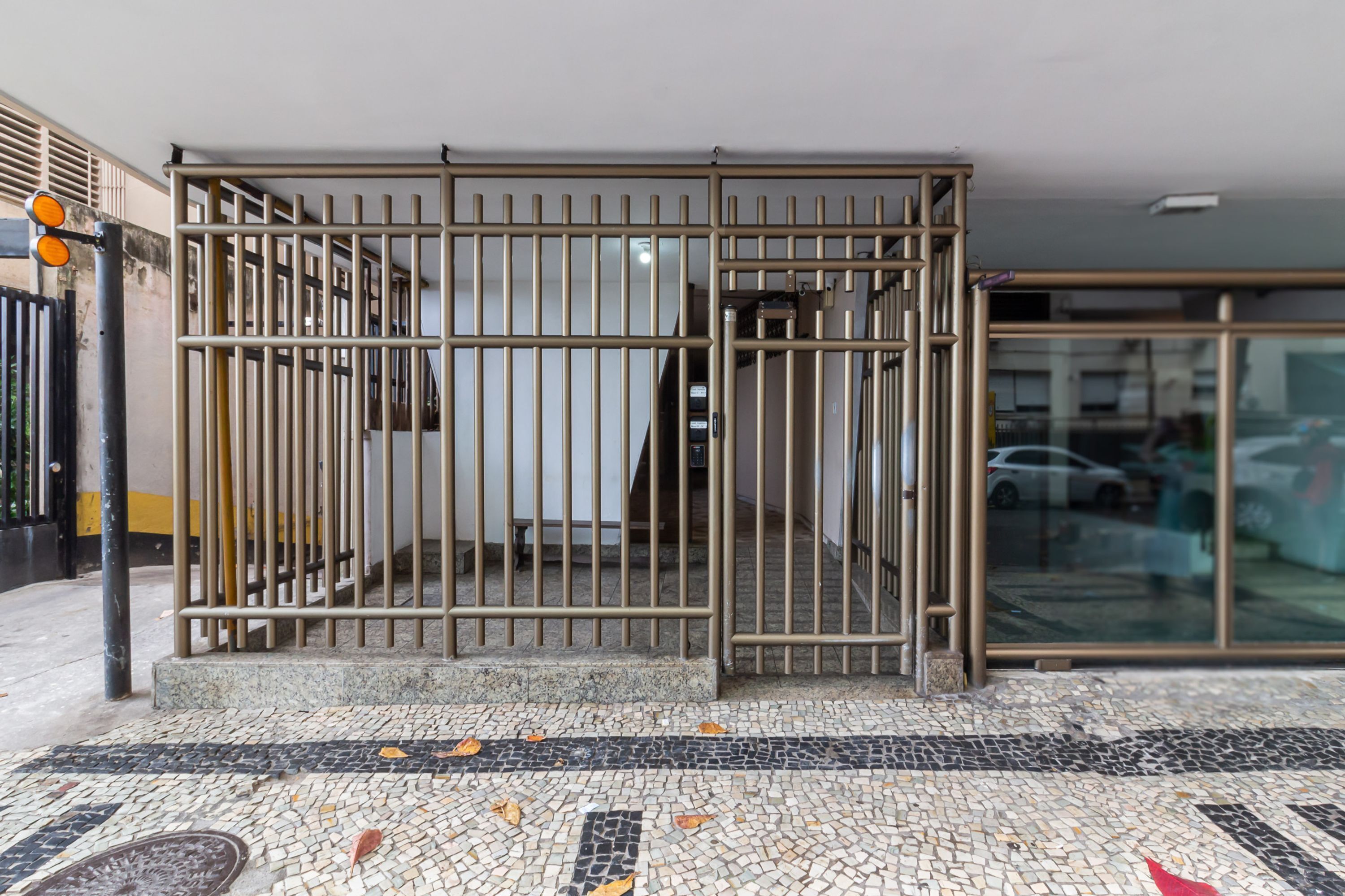 A gated entrance with a metal gate, a tiled floor, and a glass door leading to a parking area.