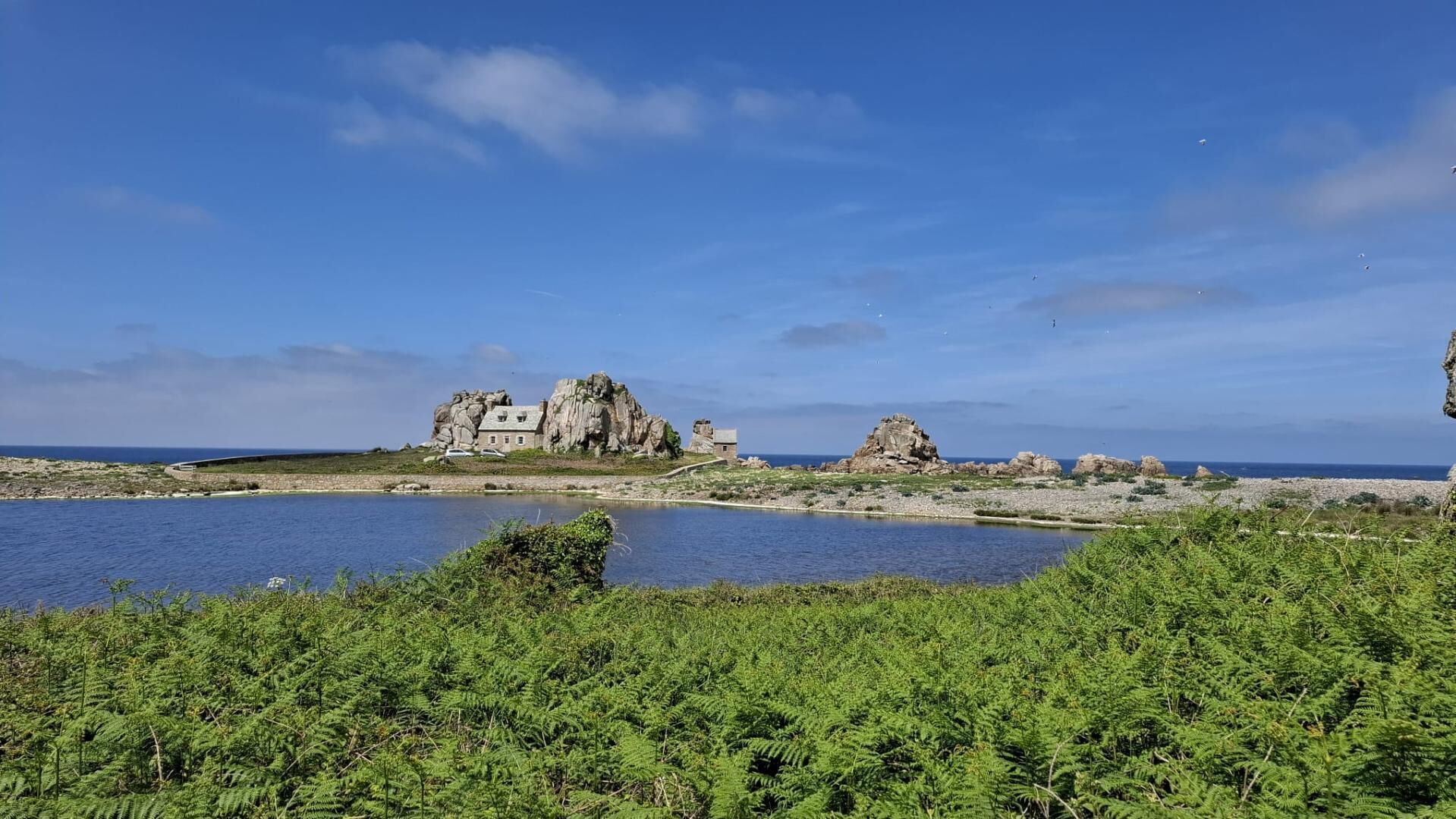 Un paysage côtier avec une grande formation rocheuse et un bâtiment doté de nombreuses fenêtres.
