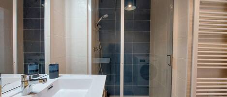 Moderni kylpyhuone, jossa on suuri valkoinen kylpyamme, lasiseinällä varustettu suihku ja pyyhekoukku.