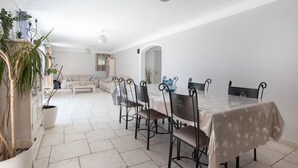 Un vaste espace de vie comprenant une table à manger, des chaises, des canapés et des plantes en pot.