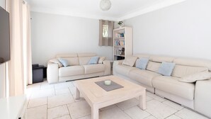 Un salon avec deux canapés beige, une table basse en bois, une bibliothèque et un téléviseur.