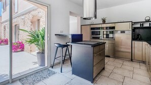 Une cuisine moderne dotée d’un îlot central, d’appareils électroménagers en acier inoxydable et donnant sur un espace extérieur agrémenté de plantes.