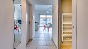 A hallway with a mirrored wall, a sliding glass door leading to a balcony, and a white radiator. - Appartement Proche Plage (La Rochelle)